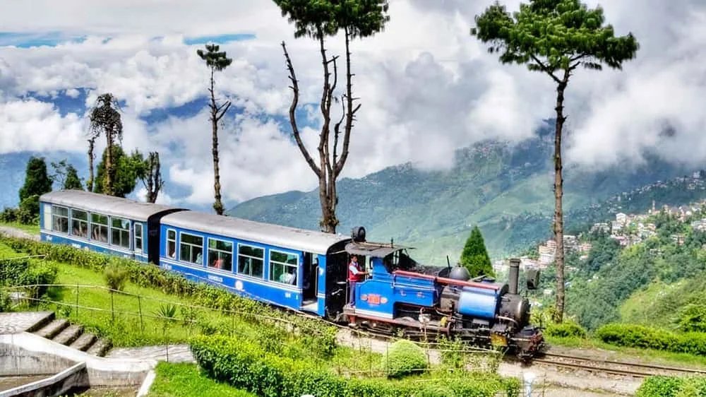 Stunning view of Darjeeling with tea plantations, the Kanchenjunga mountain range, and colonial-era architecture amidst lush greenery.